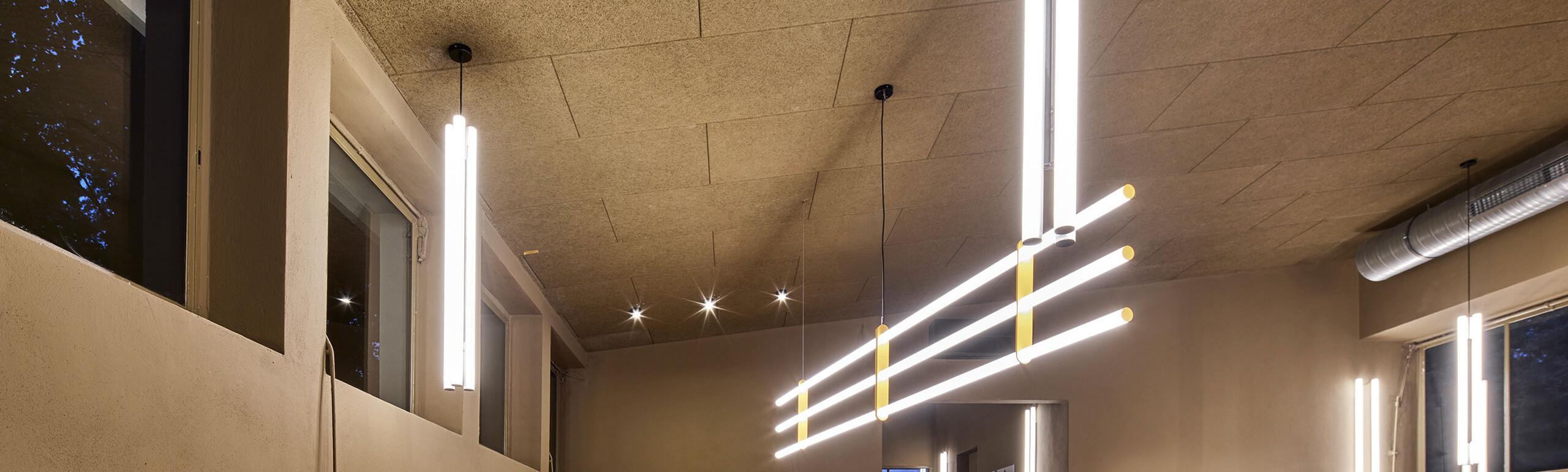Moderne Lobby mit integrierter Eventküche im Industrial Design: Geschwungene Kücheninsel aus Edelstahl, markante gelbe Fronten und minimalistische LED-Pendelleuchten.