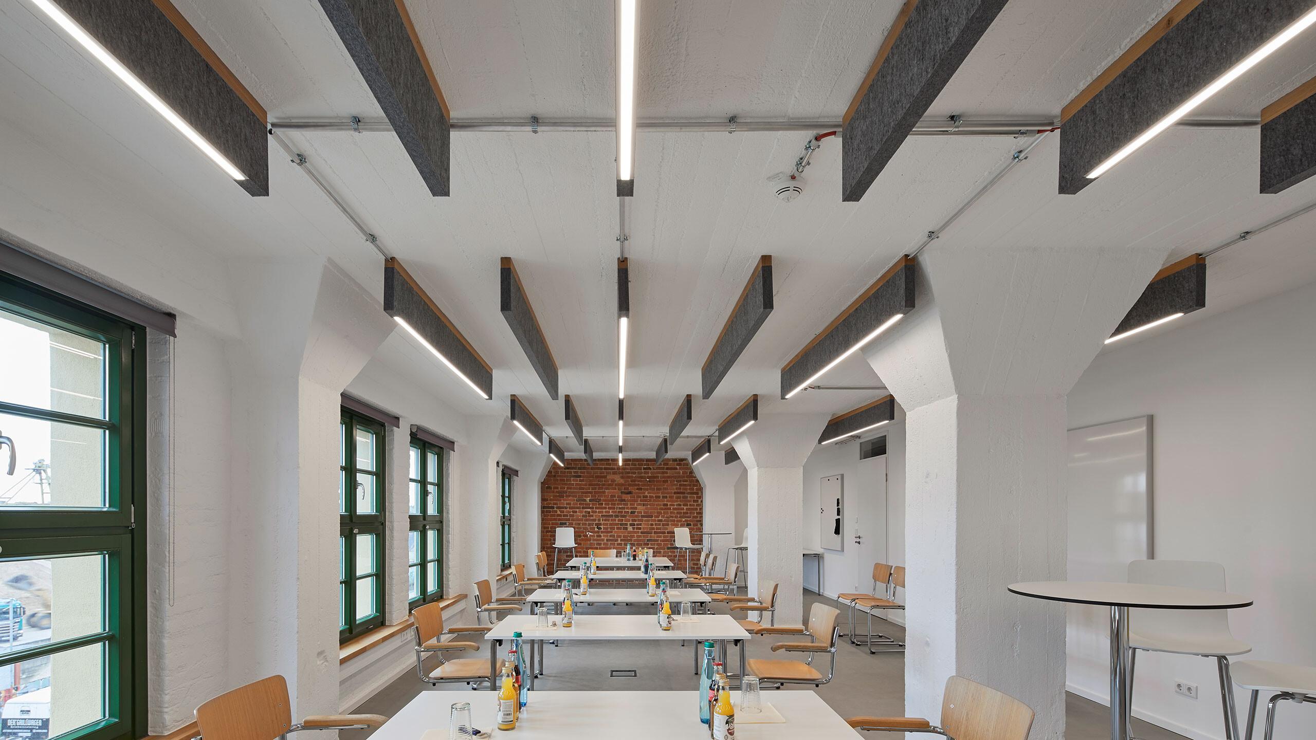 Schalldämpfendes Akustiksegel mit Beleuchtung in einer Meeting-Zone für bessere Sprachverständlichkeit.