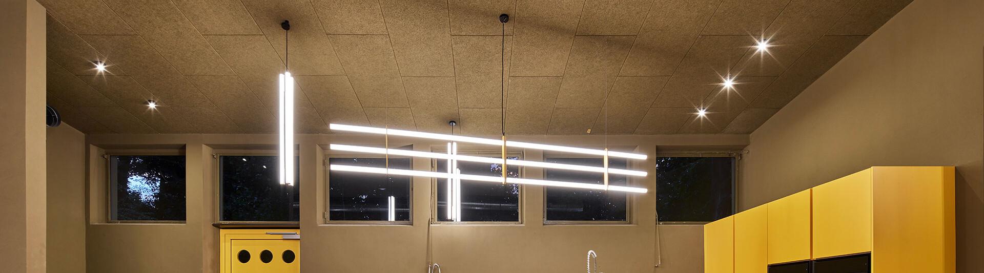 Moderne Rezeptionsbeleuchtung mit eleganten, tief hängenden Pendelleuchten über einem minimalistischen Empfangstresen in einer Lobby.